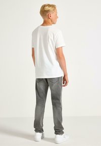 Witte katoenen t-shirt met korte mouwen, gecombineerd met grijze spijkerbroek met een lichte vervaging en twee achterzakken. Witte sneakers maken de look compleet.
