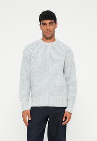 Maglione a coste grigio chiaro con scollo rotondo e maniche lunghe, caratterizzato da una vestibilità comoda e una superficie testurizzata. Abbinato a jeans scuri.