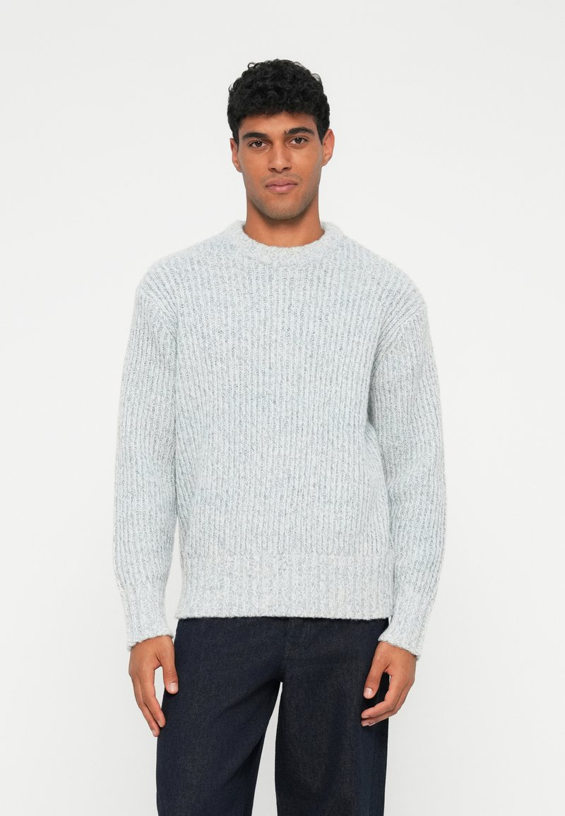 Maglione a coste grigio chiaro con scollo rotondo e maniche lunghe, caratterizzato da una vestibilità comoda e una superficie testurizzata. Abbinato a jeans scuri.