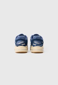Par tenisica New Balance 1000 u mornarsko plavoj i bež boji prikazanih s leđa, s vidljivim logotipom i brojem modela na peti.