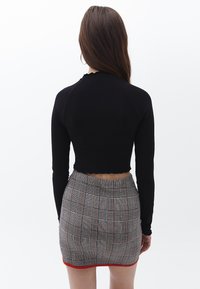 Schwarzes geripptes Langarm-Crop-Top, kombiniert mit einem grauen Karominirock mit roten Akzenten und einem dezenten gewellten Saum.