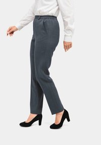 Graue Hosen mit einem elastischen Bund, ausgestattet mit zwei Seitentaschen und vertikalen Nadelstreifen, kombiniert mit schwarzen High Heels.