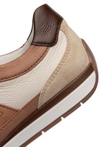 Detailní záběr na patu tenisky z hnědé, béžové a krémové kůže a semiše s bílým a hnědým gumovým detailem podrážky.