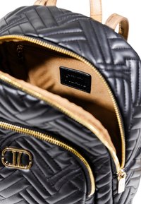 Zaino in pelle trapuntata nera con cerniere dorate e logo, scomparto principale aperto che mostra un interno beige e una piccola tasca con zip all'interno.