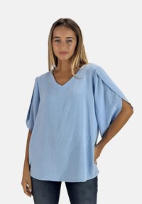 Lichtblauw oversized top met een V-hals, korte mouwen en een gestructureerde stof. Gepaard met donkere jeans voor contrast.