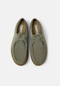 Scarpe verde scamosciato con suola in gomma marrone, caratterizzate da punta rotonda, design senza lacci e dettagli cuciti sulla parte superiore.