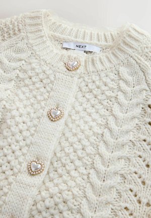 Cardigan tricotat crem cu model cu torsade, având nasturi în formă de inimă cu accente de perlă și guler cu dungi.