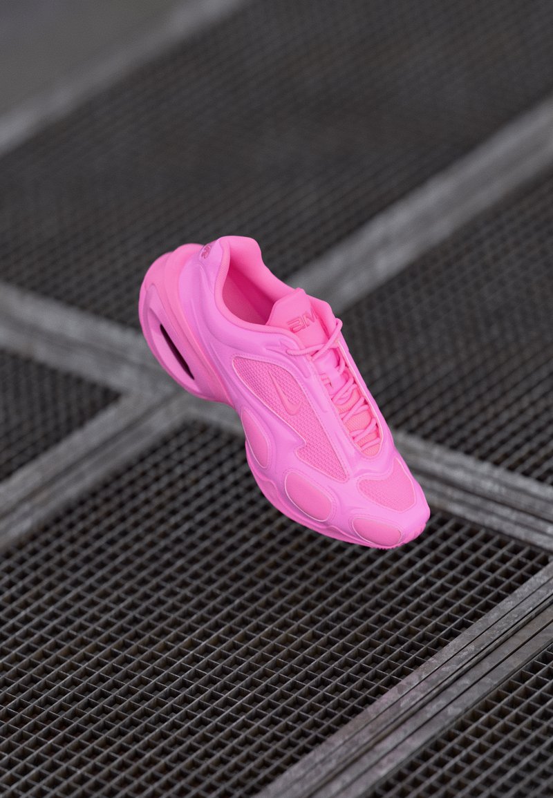 Bright pink athletic sneaker with mesh and synthetic panels, floating above a metal grid floor with a crisscross pattern.