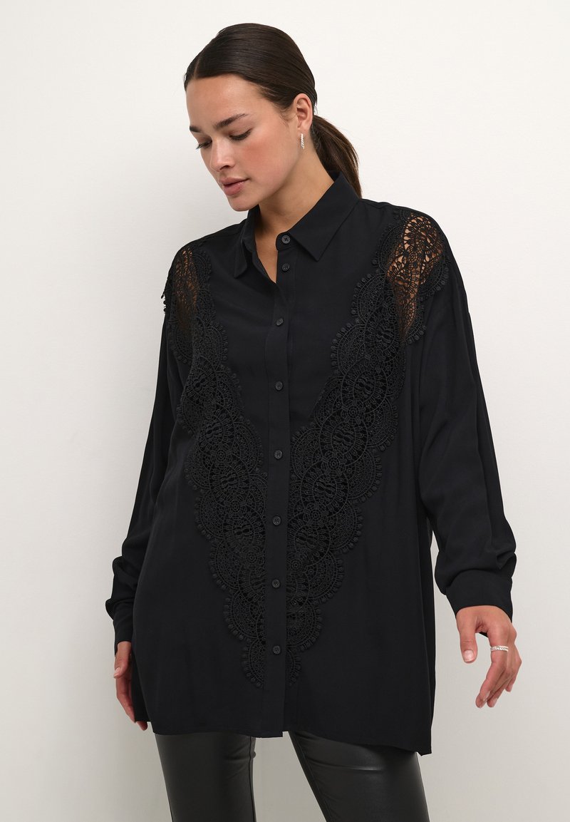 Camicia nera con bottoni, caratterizzata da intricati dettagli in pizzo sul petto e sulle spalle. Tessuto morbido, maniche lunghe e vestibilità rilassata.
