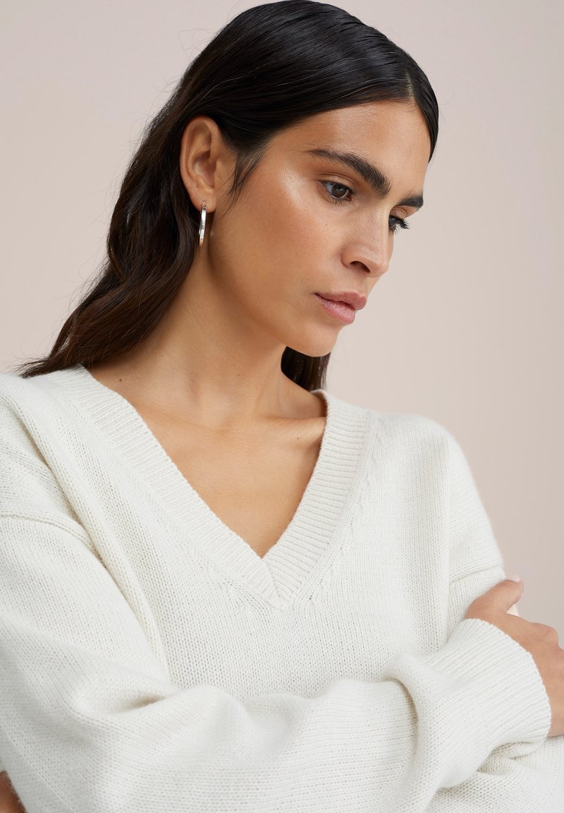 Cremfarbener Strickpullover mit V-Ausschnitt und gerippten Bündchen, der eine weiche Textur und eine lockere Passform bietet. Einfaches Design ohne sichtbare Muster.