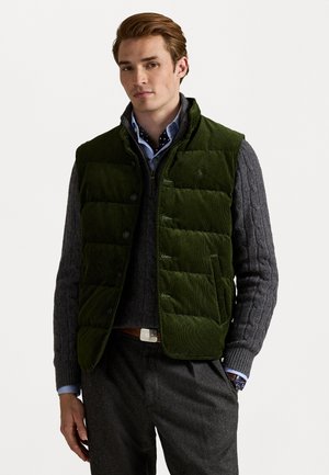 Grønne kordfløjl puffer vest med højkrave, frontknapper og sidelommer, lagdelt over en grå kabelstriktrøje og en blå skjorte.