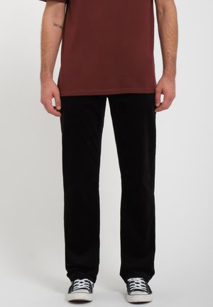 Zwarte corduroybroek met een recht gesneden ontwerp, gecombineerd met een bordeauxrood T-shirt met korte mouwen en zwarte sneakers met witte accenten.
