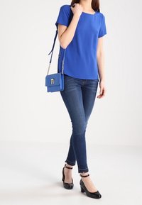 Modrá krátká blůza s čtvercovým výstřihem, nošená s tmavými skinny džíny a černými lakovými lodičkami. Malá modrá kabelka přes rameno s řetízkovým popruhem.