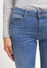 Blå denimjeans med en åtsittande design, fem fickor och en klassisk midja med metalldopp och dragkedjestängning.