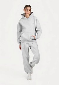 Grijze hoodie met kangoeroezak en bijpassende grijze joggingbroek. Zachte stof, ontspannen pasvorm, minimale branding en witte sneakers.