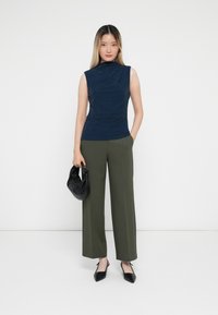 Top sin mangas en color navy con tejido texturizado, combinado con pantalones de pierna ancha en color verde oliva. El accesorio es un pequeño bolso negro y un par de zapatos de punta.