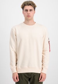 Sudadera color beige claro, material de algodón, cuello redondo, mangas largas, puños acanalados, bolsillo con cremallera en la manga izquierda, detalle en etiqueta roja.