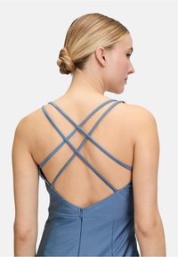 Niebieska sukienka z krzyżującymi się ramiączkami; gładki materiał, dopasowany krój i pionowe szwy na plecach; subtelne zapięcie na zamek.