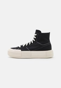 Sneakers typu high-top wykonane z czarnego płótna, ze białymi szwami i sznurowadłami. Posiadają masywną, kremową podeszwę z prostokątnymi akcentami.