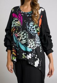 Sort, oversized top med et farverigt sommerfugleprint på forsiden, med rund halsudskæring og puffede ærmer, der smalner af ved håndleddene.