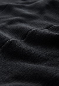 Svart tyg med mjuk textur, som har fina räfflor och subtila veck, med fokus på materialets rika djup och släta utseende.