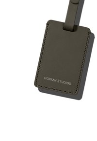 Étiquette de bagage en cuir vert foncé avec une bordure cousue, arborant une attache en boucle et le logo "HORIZN STUDIOS" embossé à l'avant.