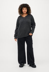 Sweater de malha cinza escuro com decote em V, mangas longas e corte descontraído, combinado com jeans pretos de perna larga e sapatos pretos robustos.