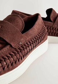 Chaussures à enfiler en suède marron avec un design tissé, semelle extérieure en caoutchouc blanc et fermeture à bande velcro. L'intérieur dispose d'un revêtement doux.