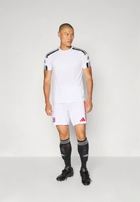 Vitt träningslinne med svarta ränder på axlarna, kombinerat med vita shorts med röda detaljer och logo, kompletterat med svarta strumpor och fotbollsskor.