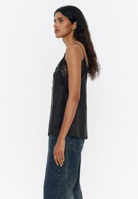 Camiseta de satén negra con detalle de encaje en los lados. Tirantes finos, corte relajado y dobladillo redondeado. Combinada con jeans azules holgados y desgastados.