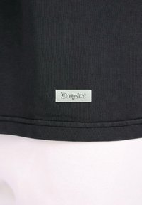 Camiseta negra de algodón con una textura suave. Presenta una etiqueta de metal con el logotipo "Dropside" cerca del dobladillo. Diseño simple y minimalista.