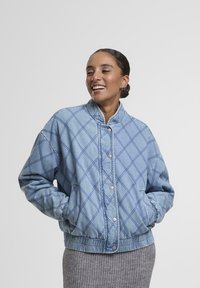 Gai zila, quiltota džinsa jaka ar elastīgām piedurknēm un jostasvietu. Tiek piedāvāta ar snap pogu aizdari un dimanta raksta dekorējumu.