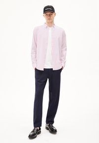 Lichtroze langemouwen shirt over een wit T-shirt, gecombineerd met een marineblauwe broek en zwarte instappers, afgewerkt met een zwarte pet met witte tekst.