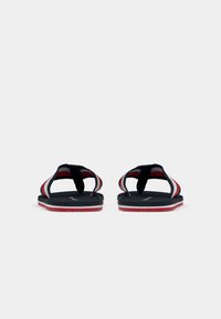 O pereche de flip-flops negre cu bretele din material în dungi roșii, albe și gri, văzute din față pe un fundal alb simplu.