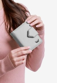 Světle šedá kožená peněženka s léga uzávěrem a černými kovovými doplňky. Kompaktní design s jemnou strukturou a vyraženým logem.
