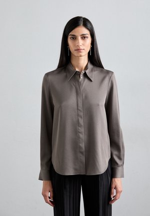 Brown silk blouse with a pointed collar, light buttons, and long sleeves. The fabric has a smooth texture, complemented by dark pleated trousers.