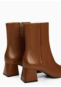 Ruskeat nahkaiset nilkkurit, joissa on neliömäinen paksu korko, takana vetoketju ja sileä, kiiltävä pinta.