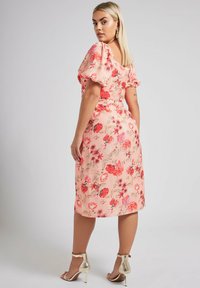Rosa blommig midiklänning med puffärmar, med en figurnära midja och ett flödande kjol. Accentuerad med röda och lila blommor, bärs med guldklackar.