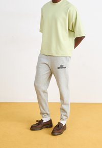 Lichtgroene t-shirt met korte mouwen, gecombineerd met grijze trainingsbroek met een zwart Nike-logo, afgemaakt met bruine schoenen en witte sokken.