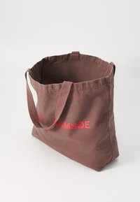 Sac en toile brun avec deux poignées en tissu et le texte "SAMSØE" en rouge vif sur le devant. Il dispose d'un intérieur spacieux et non doublé.