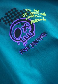 Turquoise stof met zwarte en gele geruite patronen. Grafische elementen bevatten een paarse schedel en tekst met de woorden "The Art of Creating Something Awesome."