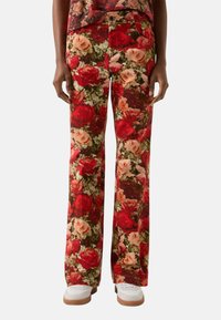 Flared pants in a floral pattern, featuring red, pink, and green roses on a brown background. Made from soft fabric with a smooth texture.