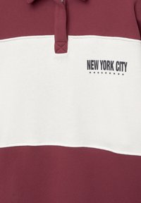 Polo a maniche corte bordeaux e bianco con colletto. Presenta la scritta "NEW YORK CITY" e un motivo a stelle sopra il testo. Tessuto di cotone morbido.