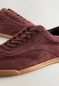 Burgundy suede sneakers with a textured finish, flat laces, and rubber soles. Features sleek lines and a low-profile design.