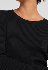 Maglione nero a coste con scollo rotondo. Le maniche lunghe presentano una finitura testurizzata, evidenziando un design aderente.