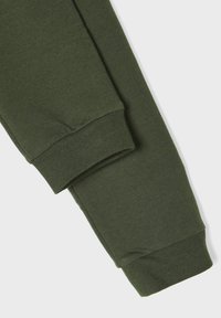 Pantaloni sport din bumbac verde închis, cu manșete striate și textură netedă. Designul prezintă un picior conic și un stil minimalist.