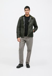 Zelená, lehká bunda s předním zipem, velkým límcem a károvanou podšívkou, v kombinaci s šedými kalhotami a černými botami.