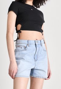 Černý žebrovaný crop top se zavazováním na bocích, doplněný světle modrými džínovými šortkami s předními kapsami a klasickým zapínáním na knoflíky.
