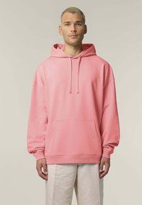 Felpa rosa realizzata in materiale morbido, con una tasca frontale, cappuccio con cordino e polsini a coste, abbinata a pantaloni leggeri e strutturati.