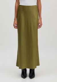 Olijfgroene maxi-rok van gladde stof, met een lange, vloeiende silhoette. Gekleed met spitse zwarte enkellaarsjes.